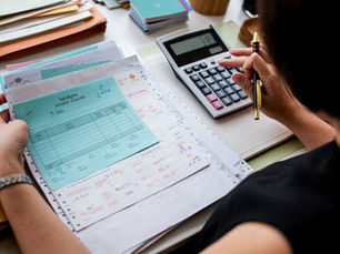 Person reviewing documents with a blue payment voucher, using a calculator on a desk. Papers, folders, and a pen are present.