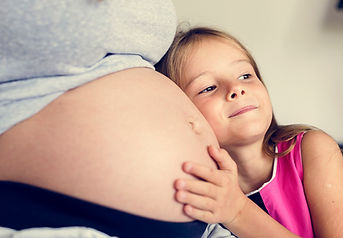 little girl with her head on a woman's pregnant belly listening to the unborn baby's heartbeat