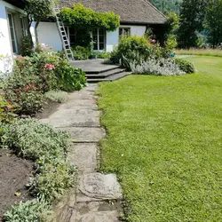 Gepflegter Privatgarten mit Rasenfläche, Natursteinweg und blühenden Staudenbeeten nach professionel