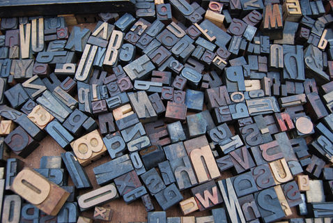 A loose random collection of used wooden letterpress letter blocks spread out on a table. Various sizes and types of font on display in the collection.