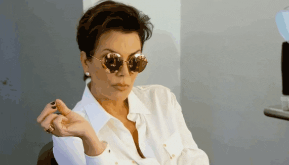 Middle aged woman in white button shirt wearing sunglasses in cool judgmental pose.
