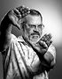 Photographer Shayne Blaylock in a black-and-white self-portrait, framing a shot with his hands in a studio-lit portrait.