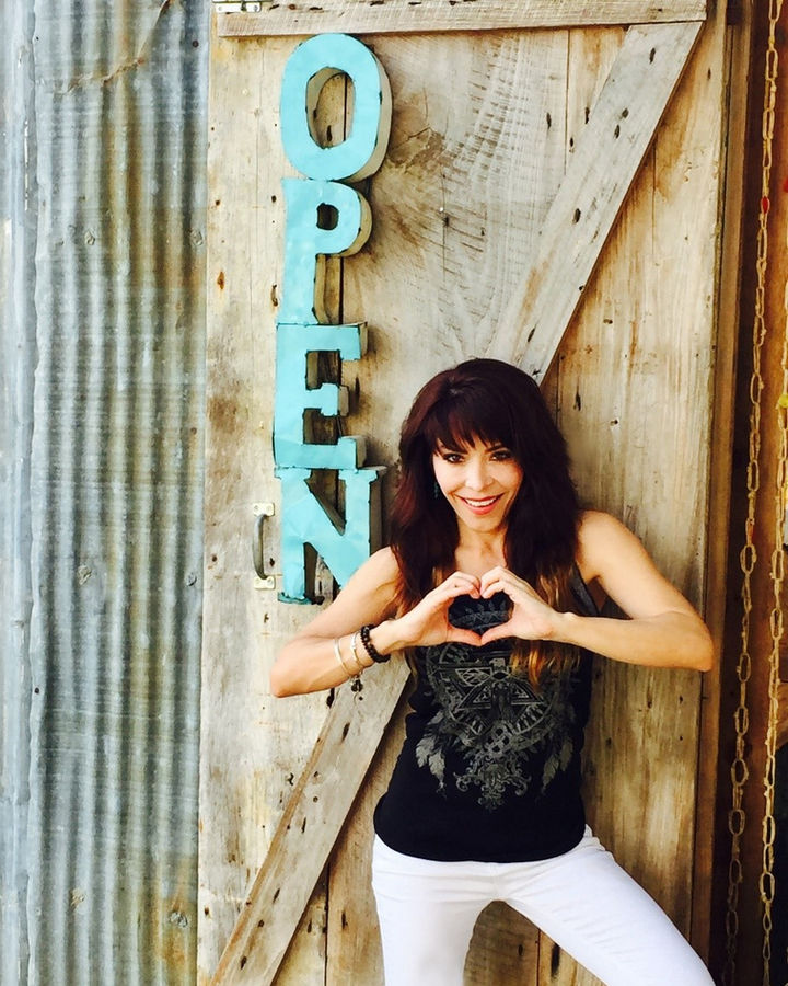 Janie making a heart with her hands in front of a door marked OPEN
