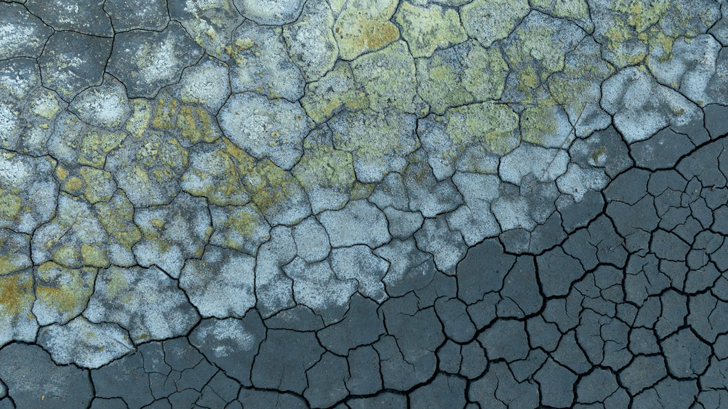 Drone image above the geothermal mud pools of Hverir in northern Iceland, showing cracked, dried earth and abstract textures shaped by geothermal activity.