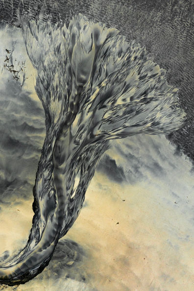 Drone image of glacier water streaming into the sea along a beach in northern Iceland, forming abstract patterns in the sand that resemble the shape of a flower.