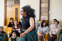 expressing, moving an actor is animated. he has curly back hair. the audience looks on