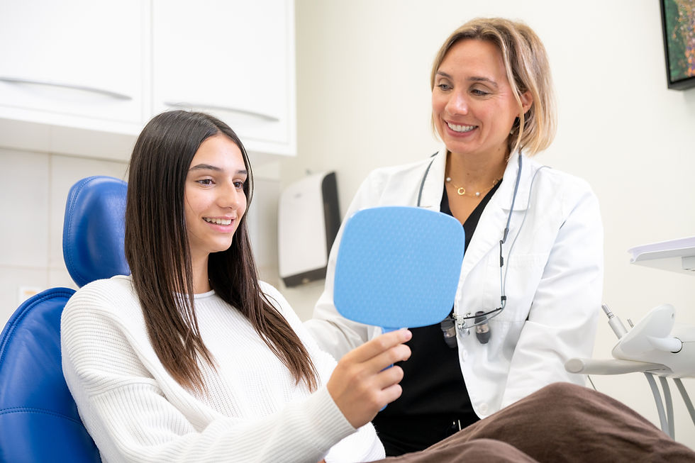 Dentist shows a young patient a mirror to see her healthy smile at the Ultimate Smile Dentistry clinic