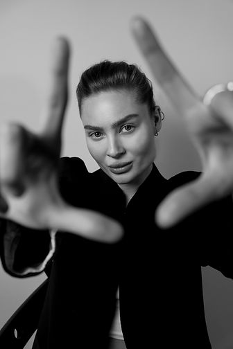 A black-and-white photo of a woman in a blazer posing playfully, reaching out toward the camera with both hands, creating a dynamic and engaging composition.