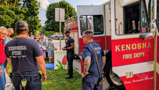 A Kenosha Fire Department fire engine parked on the street with firefighters chatting with attendees