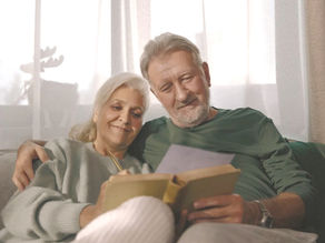 Older couple sitting on a couch, happily reading together