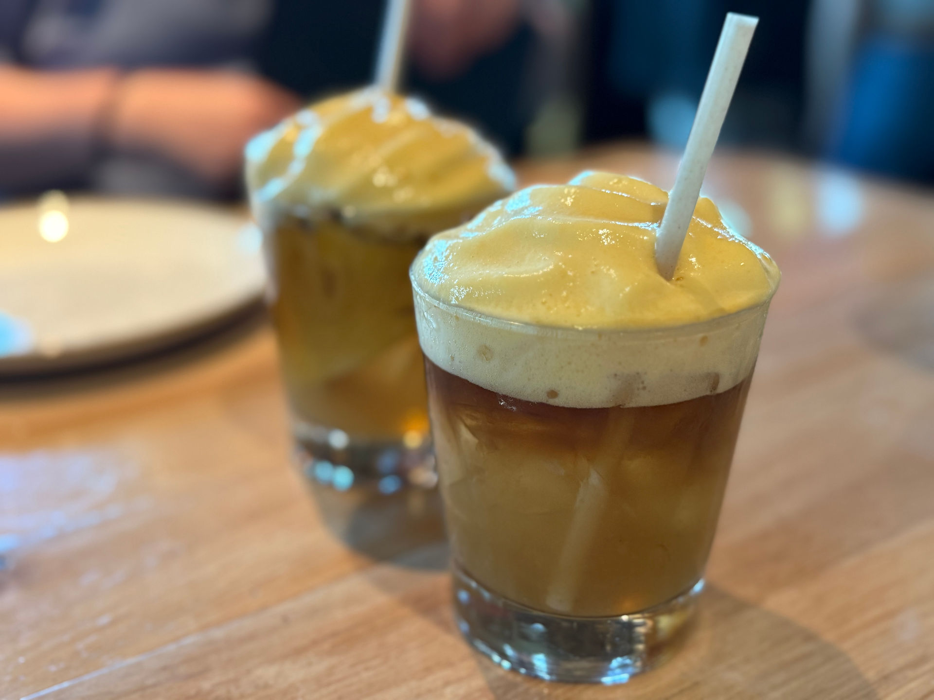 Two layered drinks with creamy yellow foam and straws.