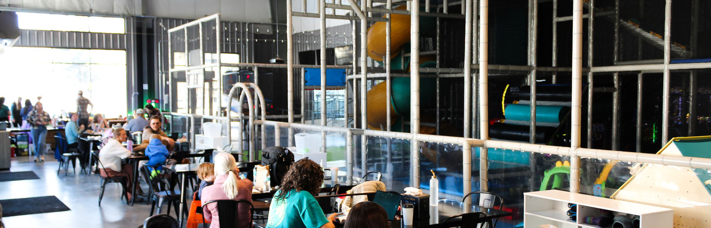 Indoor play area with people dining and playground structure