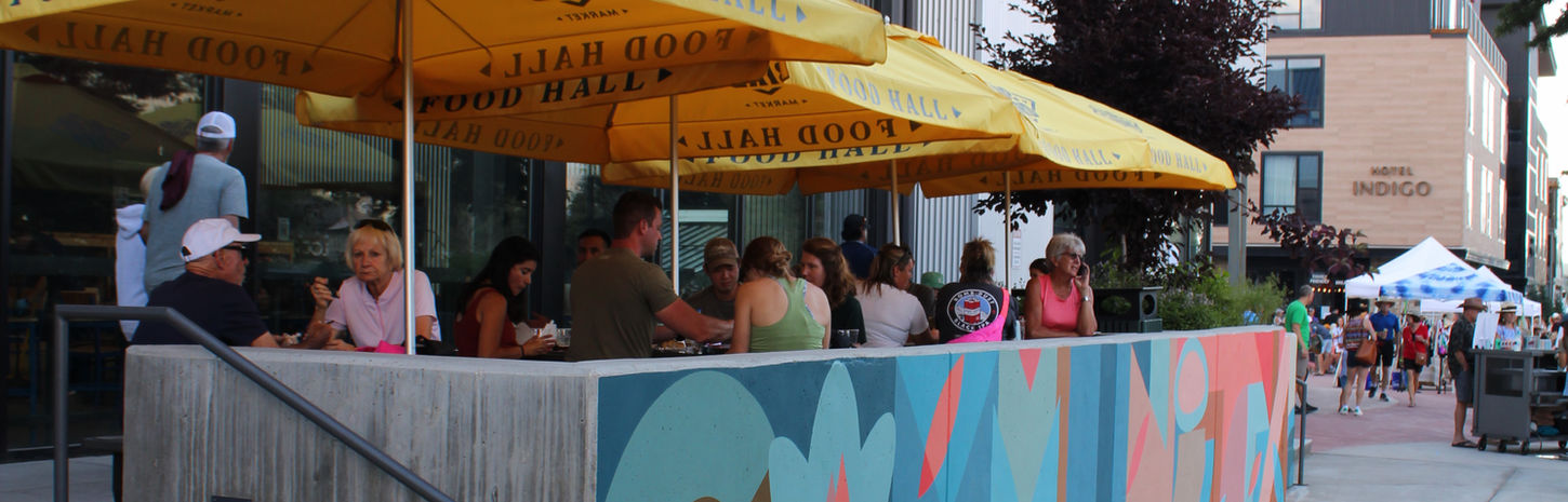 Outdoor patio with diners, yellow umbrellas, and colorful wall mural