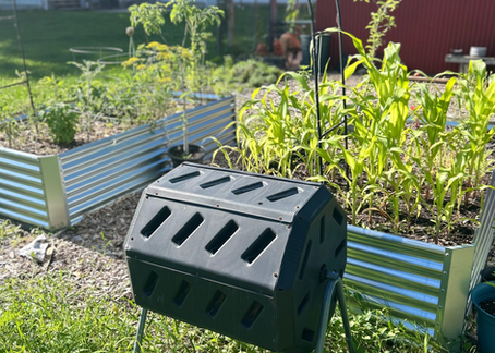 a spinning compost bin next to two raised garden beds full of plants