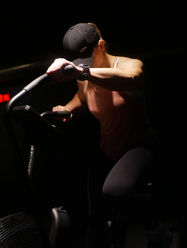 Workout attire intensely pedals a stationary bike in a dimly lit gym