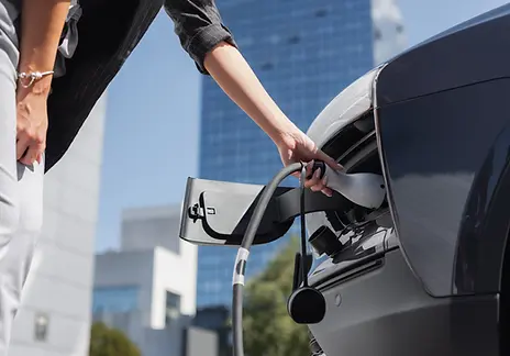 A woman is charging an electric car at a charging station, focused on connecting the charging cable.