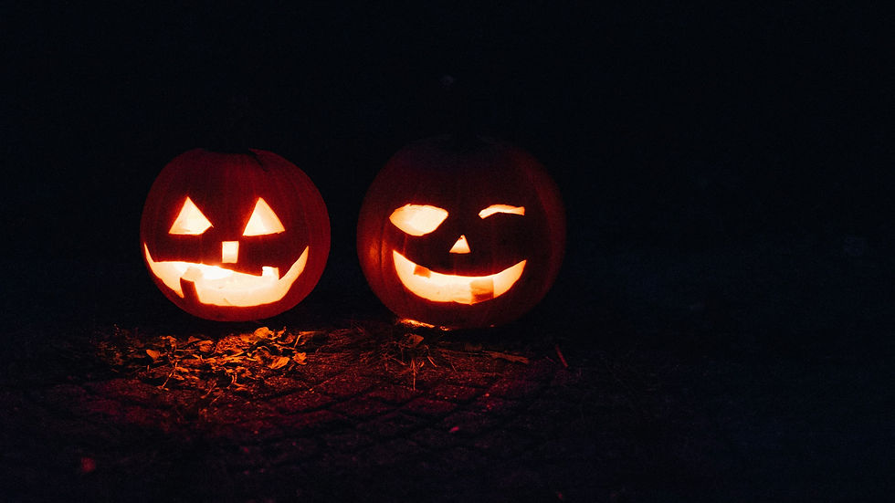 Two glowing carved jack-o'-lanterns with spooky faces sit side by side in the dark, ready for Halloween night.
