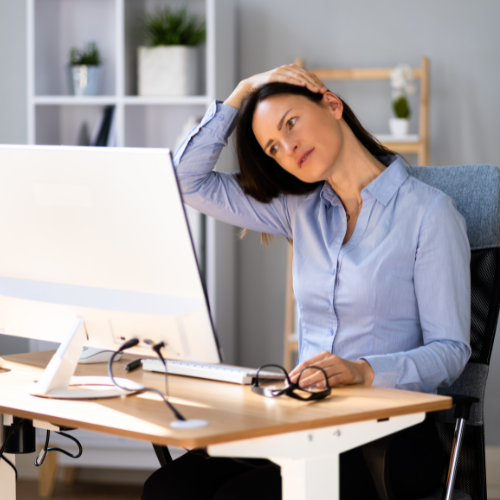 An office worker sitting at their desk doing a subtle neck stretch exercise to help with neck and back tension.