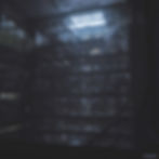 Dimly lit industrial scene with people on multiple floors, surrounded by pipes and machinery. Overhead light creates a moody atmosphere.