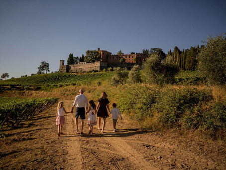 Family walking through vineyard rows at golden hour with a Tuscan villa in the background.