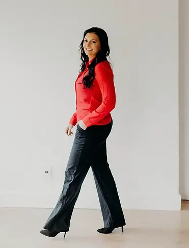 Tracey Joss, financial wellness strategist at Dream Tracer, standing in a modern setting wearing a red blouse and black trousers. Expert in financial planning and management.