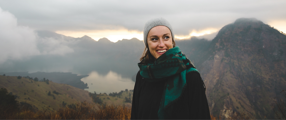 Woman smiling confidently outdoors on a hilltop with a scenic view behind her