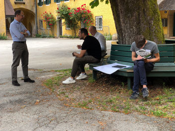 Kursteilnehmer sitzen im freien unter einem Baum uns erarbeiten gemeinsam etwas