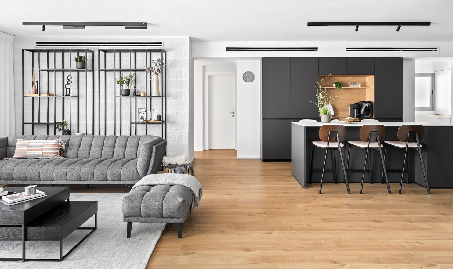 סלון ומטבח פתוח כיחידה אחת מעוצב בצבעים הרמוניים של עץ וגוונים שונים של אפור, אזור שנעים להיות בו