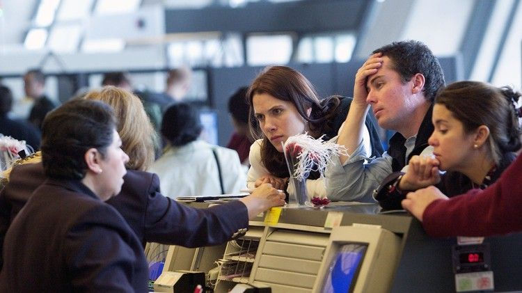 People at an airport counter appear frustrated, talking to a staff member. The setting is busy, with neutral colors and computer screens.