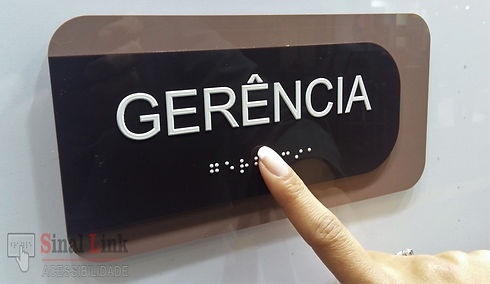 Placa de braille com texto gerência sendo tocado por dedo de uma mulher