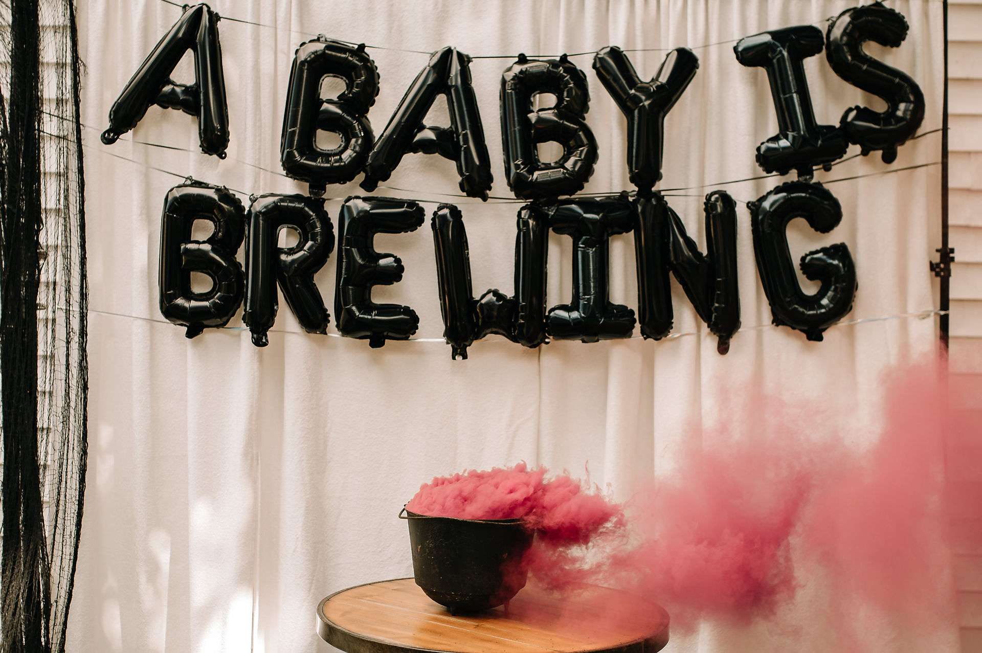gender reveal setup with a sign that reads: "A baby is brewing" and pink smoke coming out of a cauldron