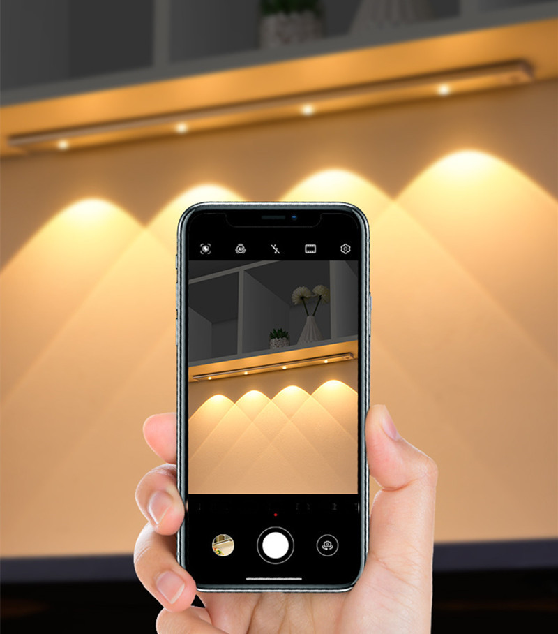 Hand holding a smartphone showcasing smart automation app features with wireless motion sensor LED lights in the background.