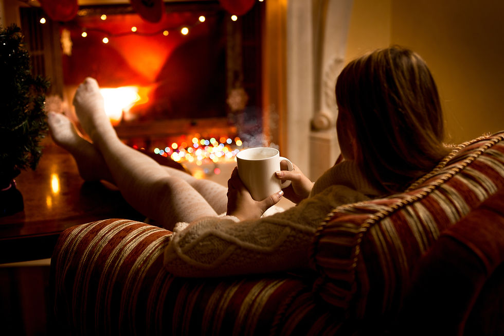 A woman relaxing by a cozy fireplace, holding a warm mug in her hands, with soft lighting and festive holiday decorations in the background.