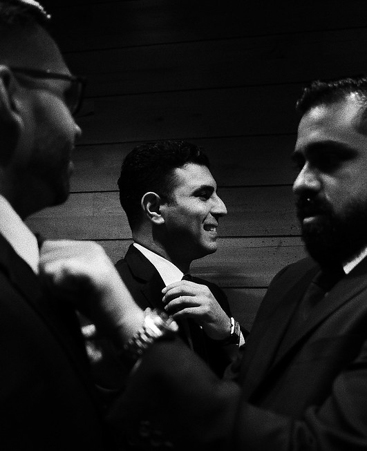 Candid black and white film photo of groomsmen adjusting suits before the ceremony, capturing fine-art documentary wedding.