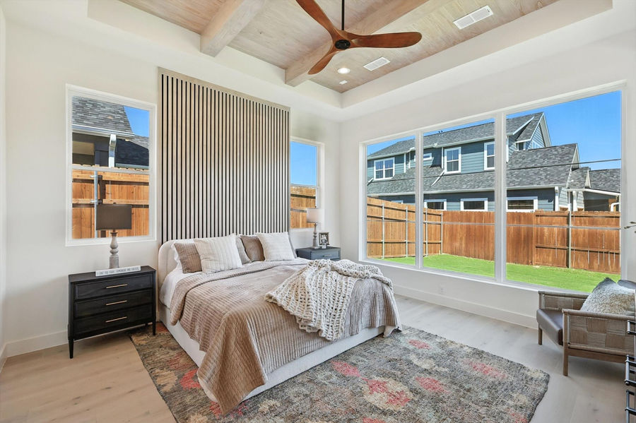 Modern master bedroom with a wood panel accent wall, natural light from three large windows, a light-colored wood bed frame, and a soft rug, showcasing a serene and stylish space.