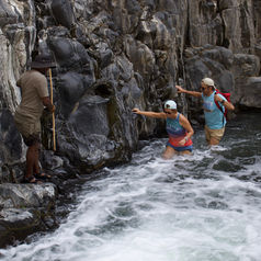 Two people walking through a canyon and a guide awaiting them on a rock