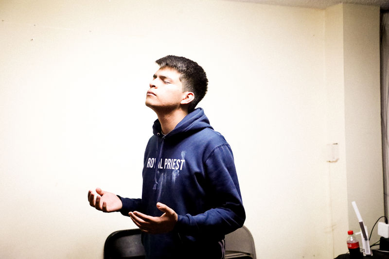 Un joven ora con los ojos cerrados y las manos abiertas, en REBORN 2024