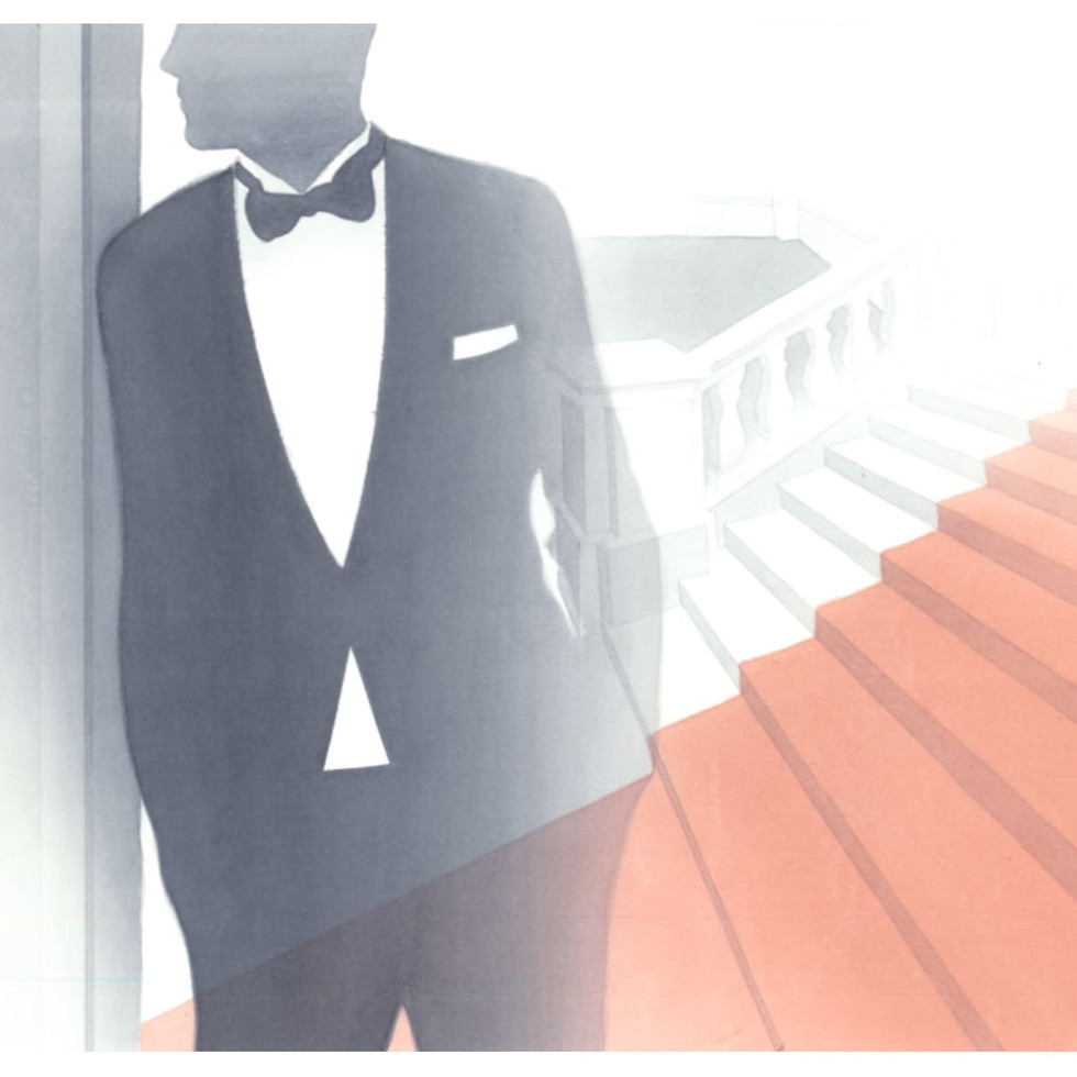 Man in a tuxedo standing by a grand staircase.