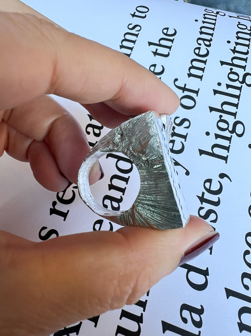 Silver signet with off-centre emerald-cut pink stone and small structural block holding it.