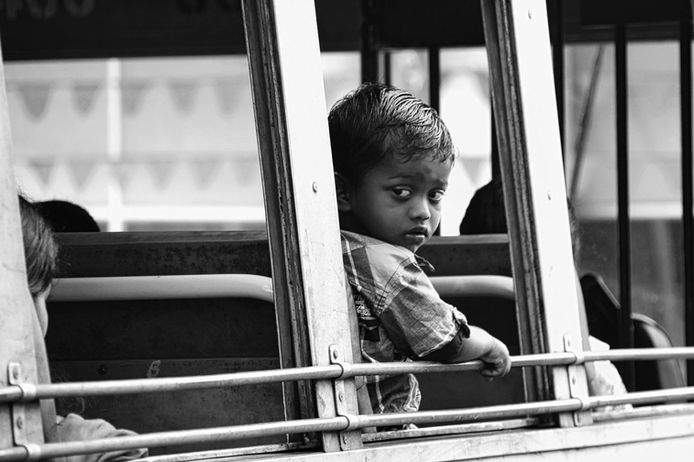 Ein erwachsen-wirkender Junge sitzt am Fenster eines Buses und schaut auf die Straßen Dehlis