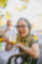 An elderly woman in colourful clothing drinking a cup of coffee happily.