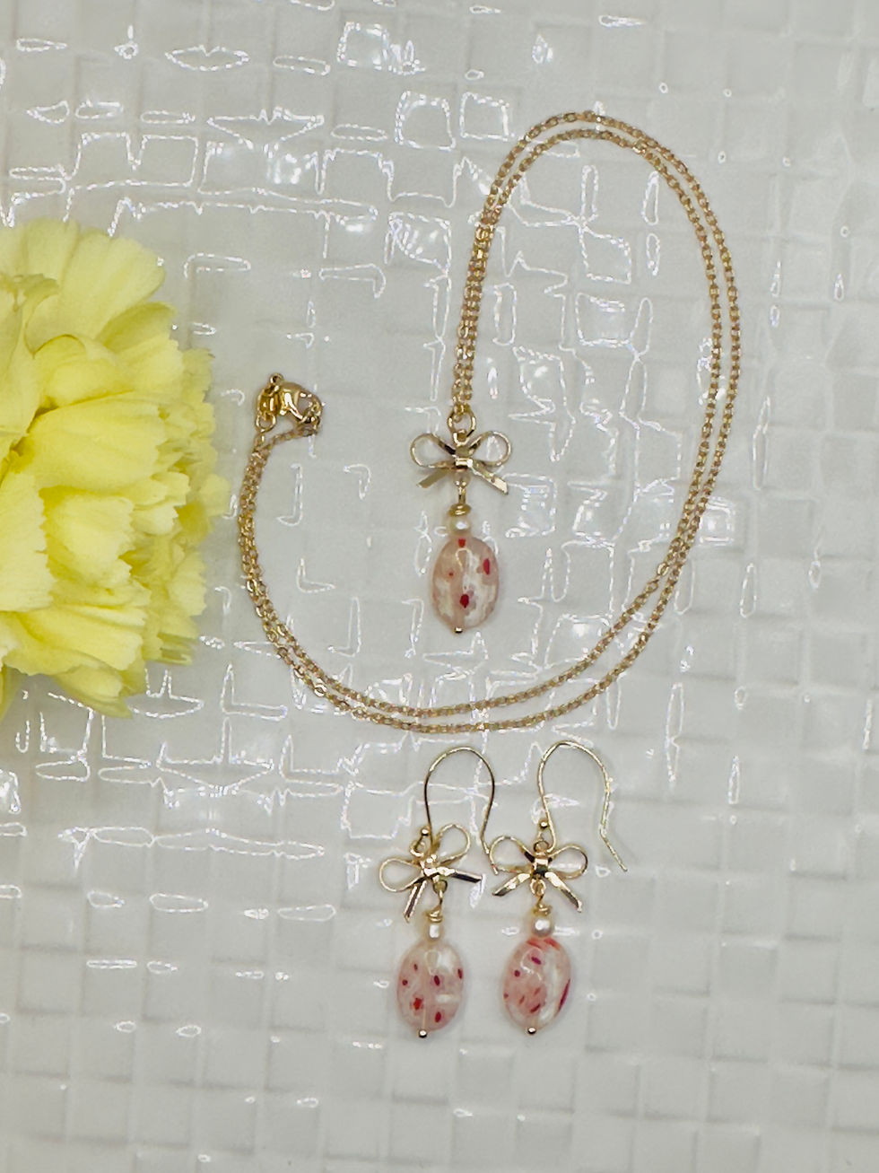 Thumbnail: Gold necklace and earrings with pink floral teardrop pendants on light background.