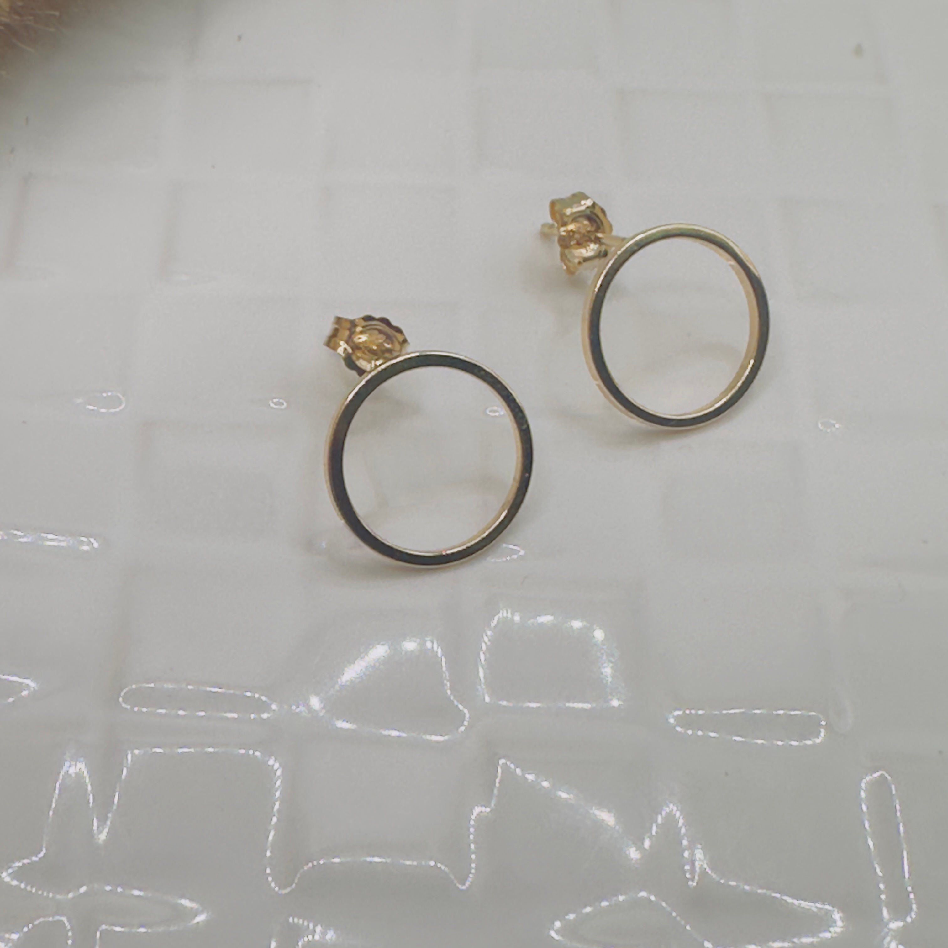 Pair of gold earrings with a black outline; white background