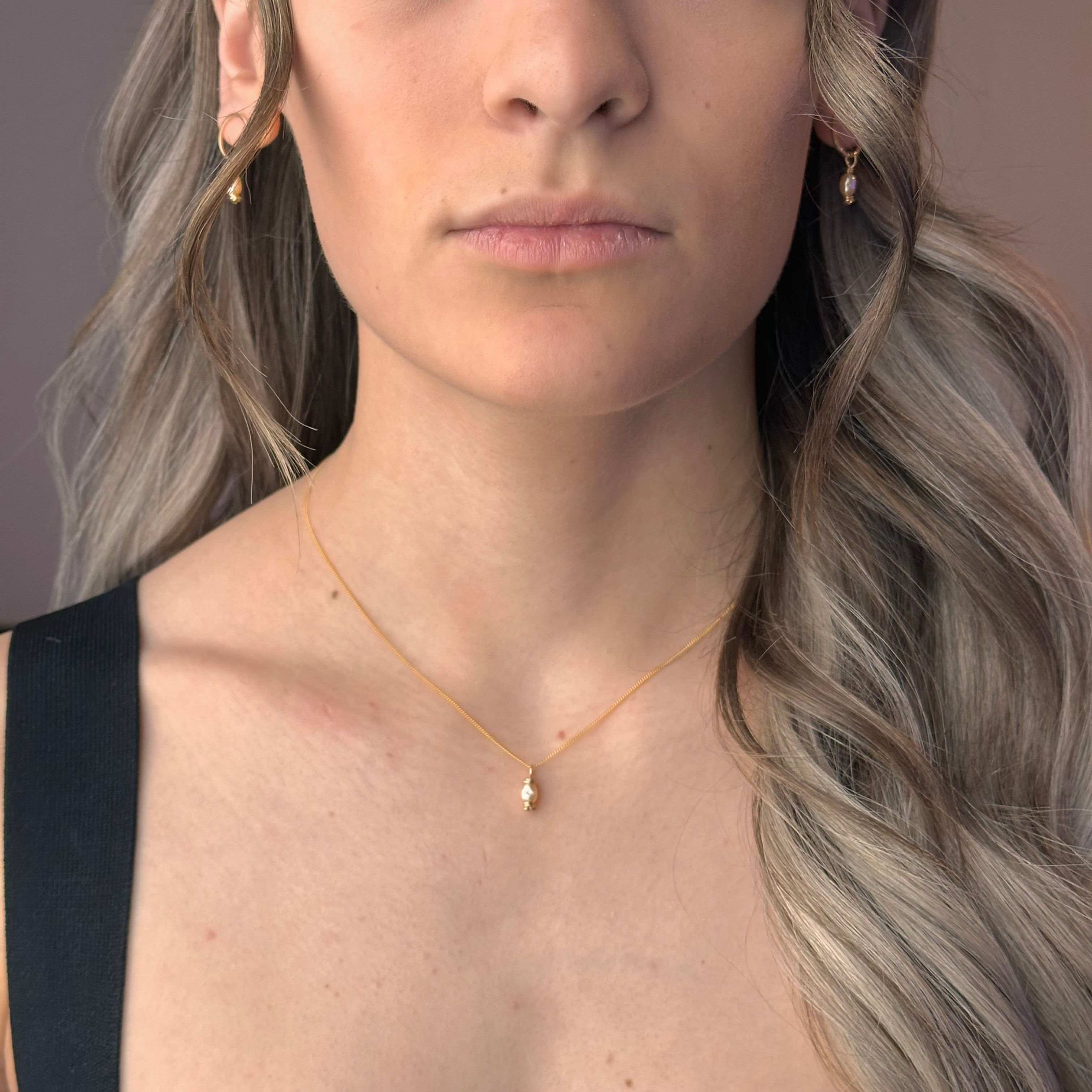 Woman models delicate gold chain necklace and matching pearl earrings.