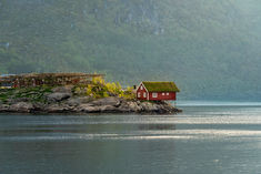 A traditional red boathouse on stilts with a grass‑covered roof, set beside classic stockfish racks in Reine. The mix of coastal architecture and fishing heritage creates an authentic glimpse into everyday life on the Lofoten Islands.