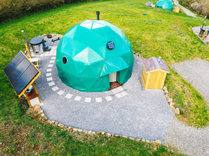 A photo of a glamping camp in Wales, showing three geodesic domes and hot tubs.