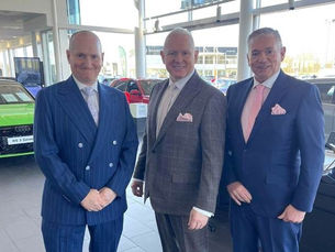 A family run motor dealership, report profits up. Three very pleased Director and brothers stand together in their showrooms.