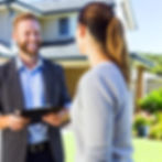 A friendly and professional roofing contractor talking to a customer in front of a house. The contractor holds a clipboard, smiling, while the customer looks pleased. The scene conveys trust, excellent customer service, and a sunny, well-maintained environment.