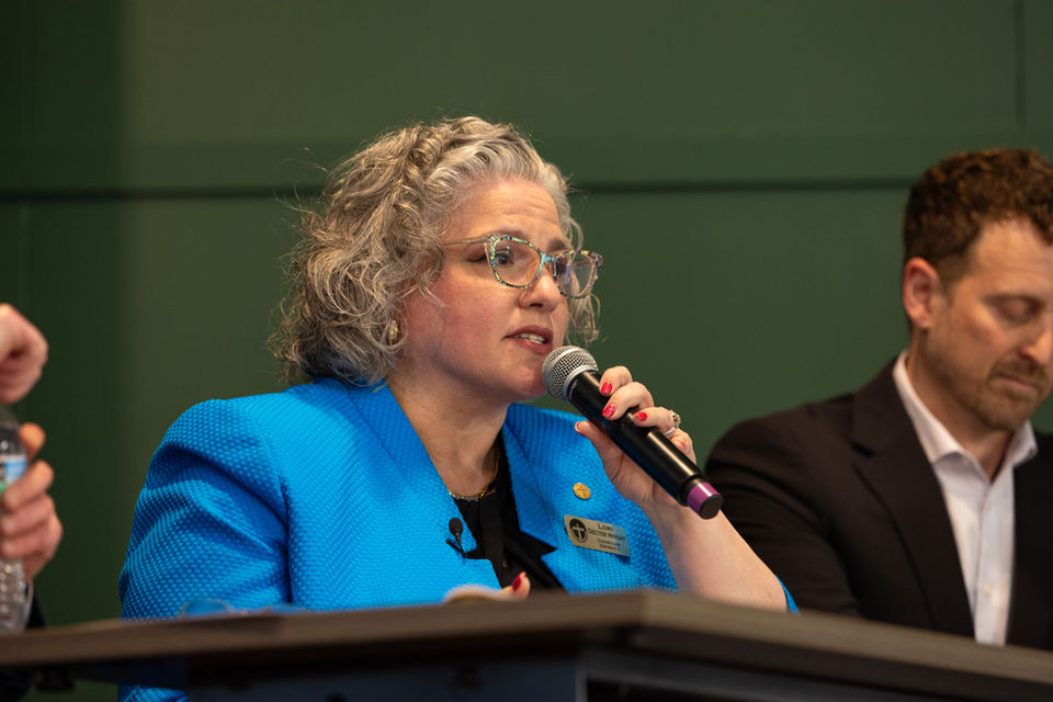 Councilor Lori Decter Wright sitting at a table on stage with a microphone and speaking alongside other elected officials at a community conversation event.