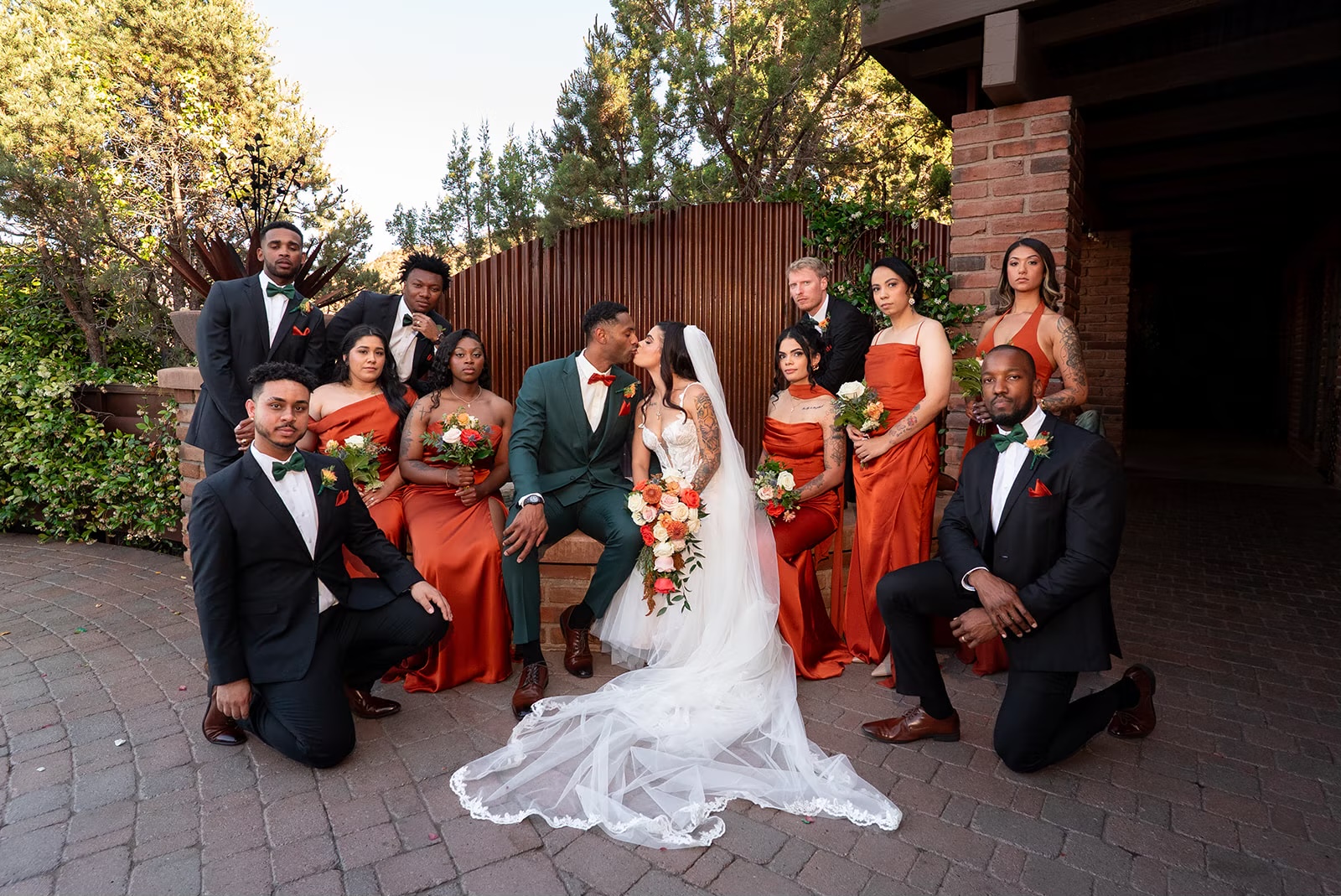 Newlyweds with their wedding party in rust-orange dresses and dark suits at an outdoor Sedona venue